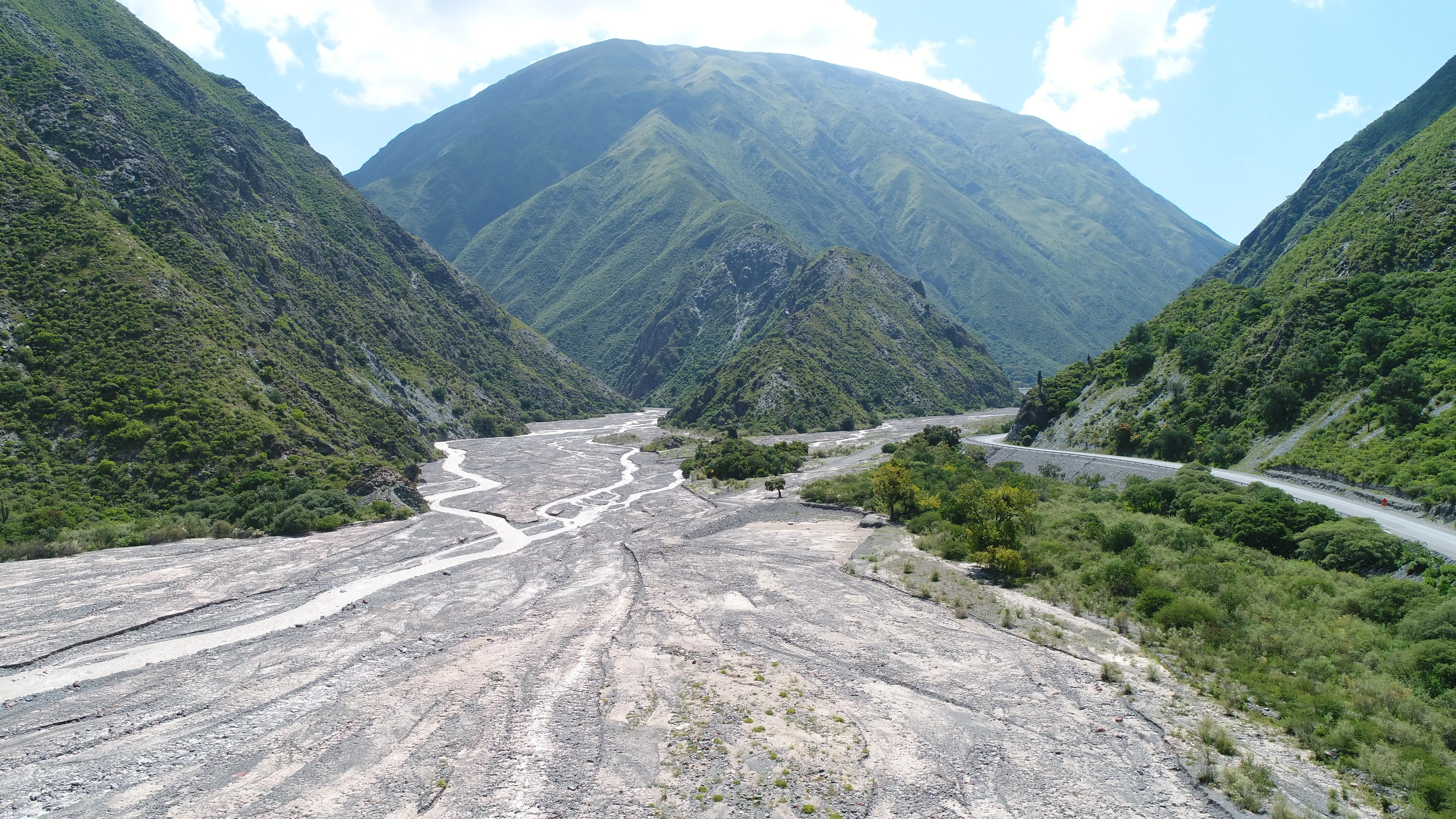 A wide, braided gravel riverbed in a steep green mountain valley
